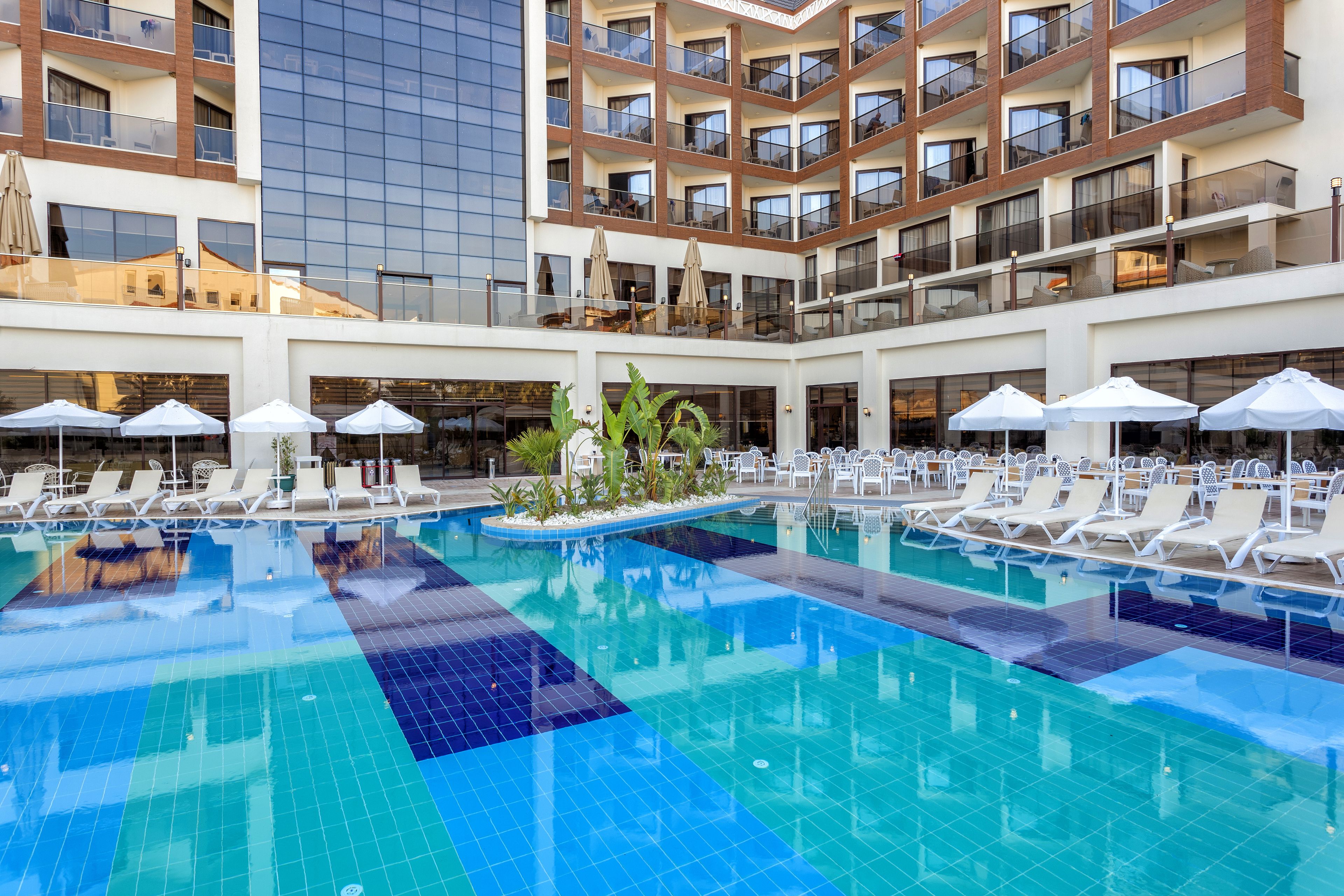 Zona de piscina hotelera con varios niveles, sillas de descanso y sombrillas.