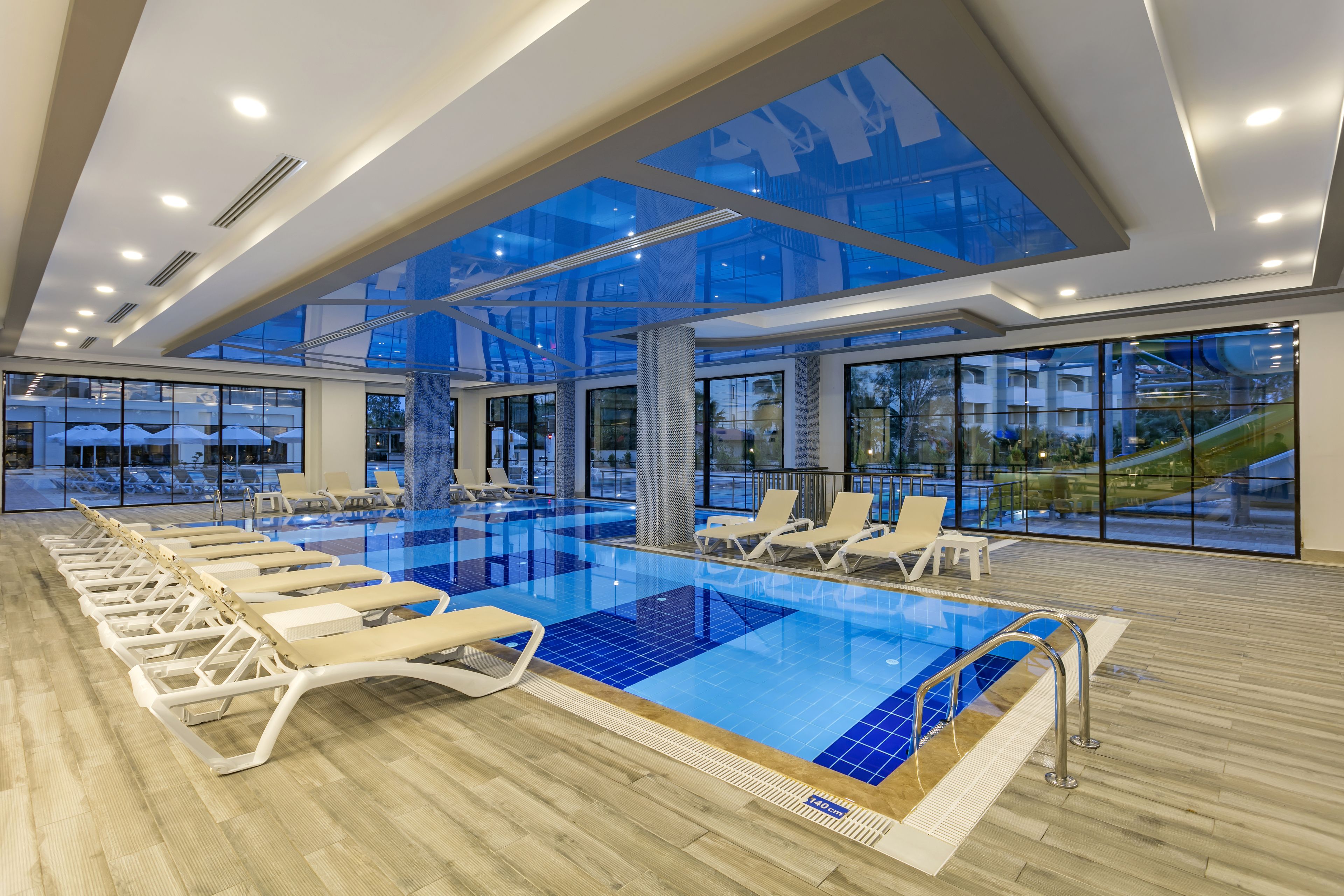 A modern indoor swimming pool with lounge chairs and large windows.