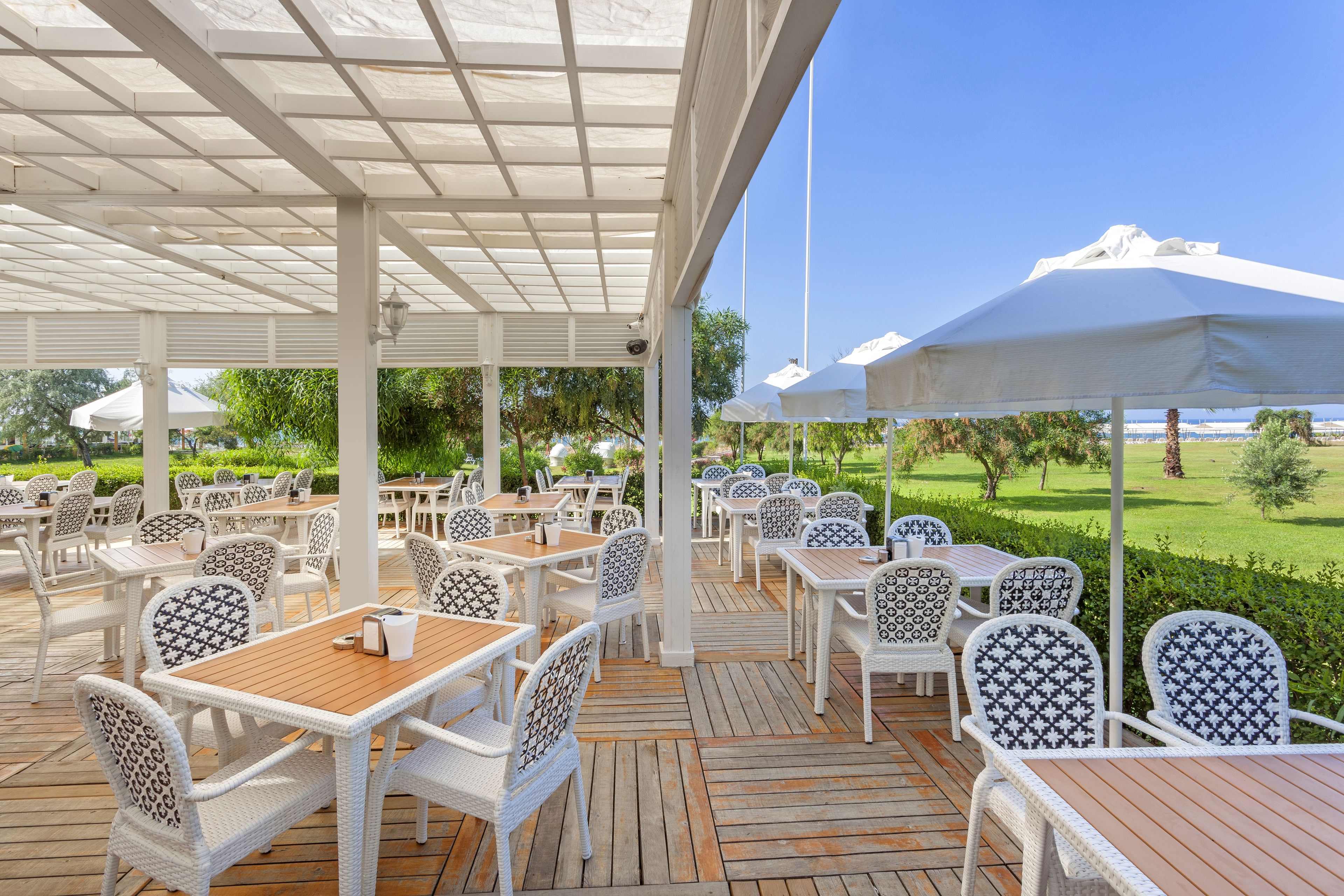 An outdoor patio area with white wicker furniture, wooden tables, and umbrellas providing shade.