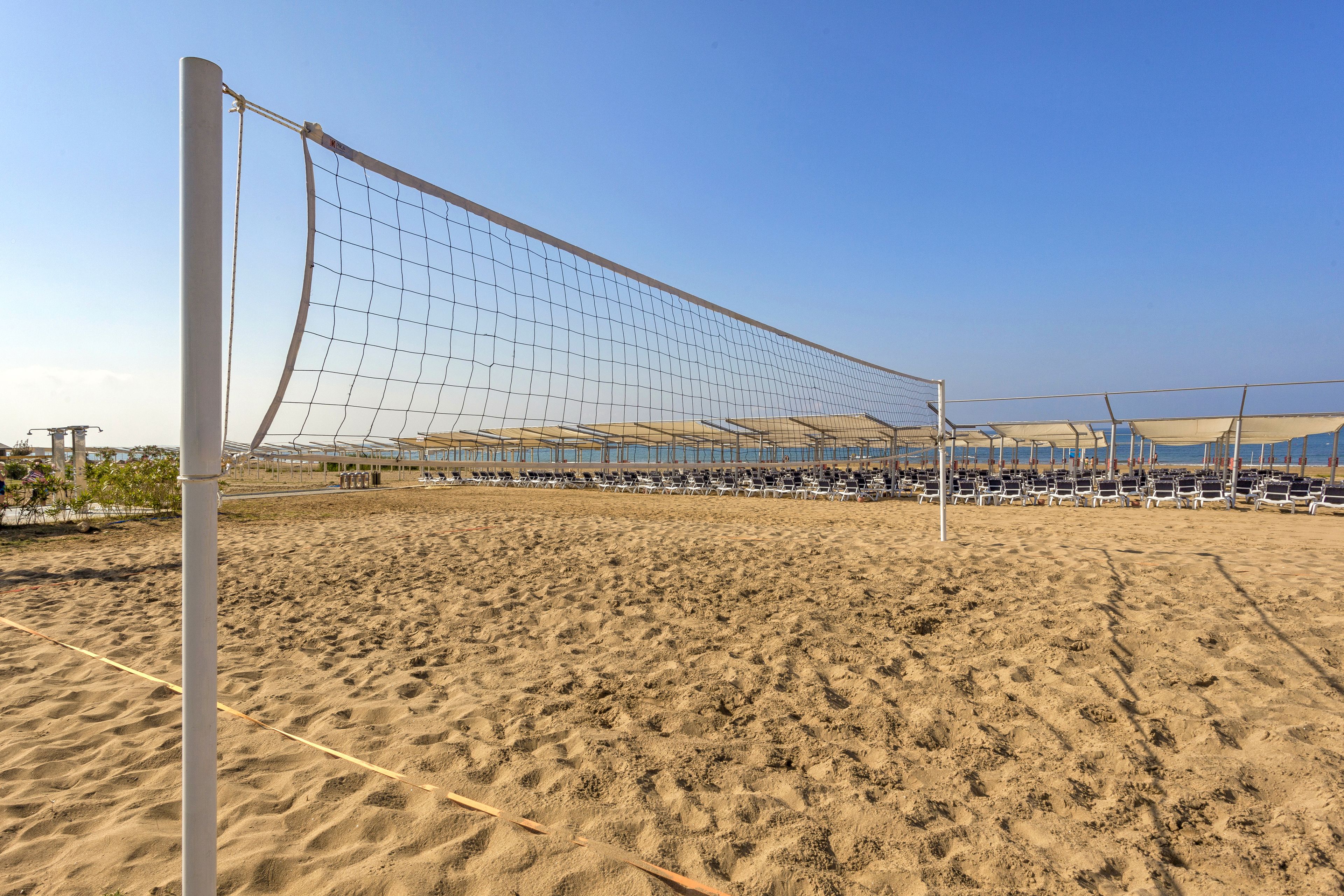 A sandy beach volleyball court with a net, chairs, and a clear sky.