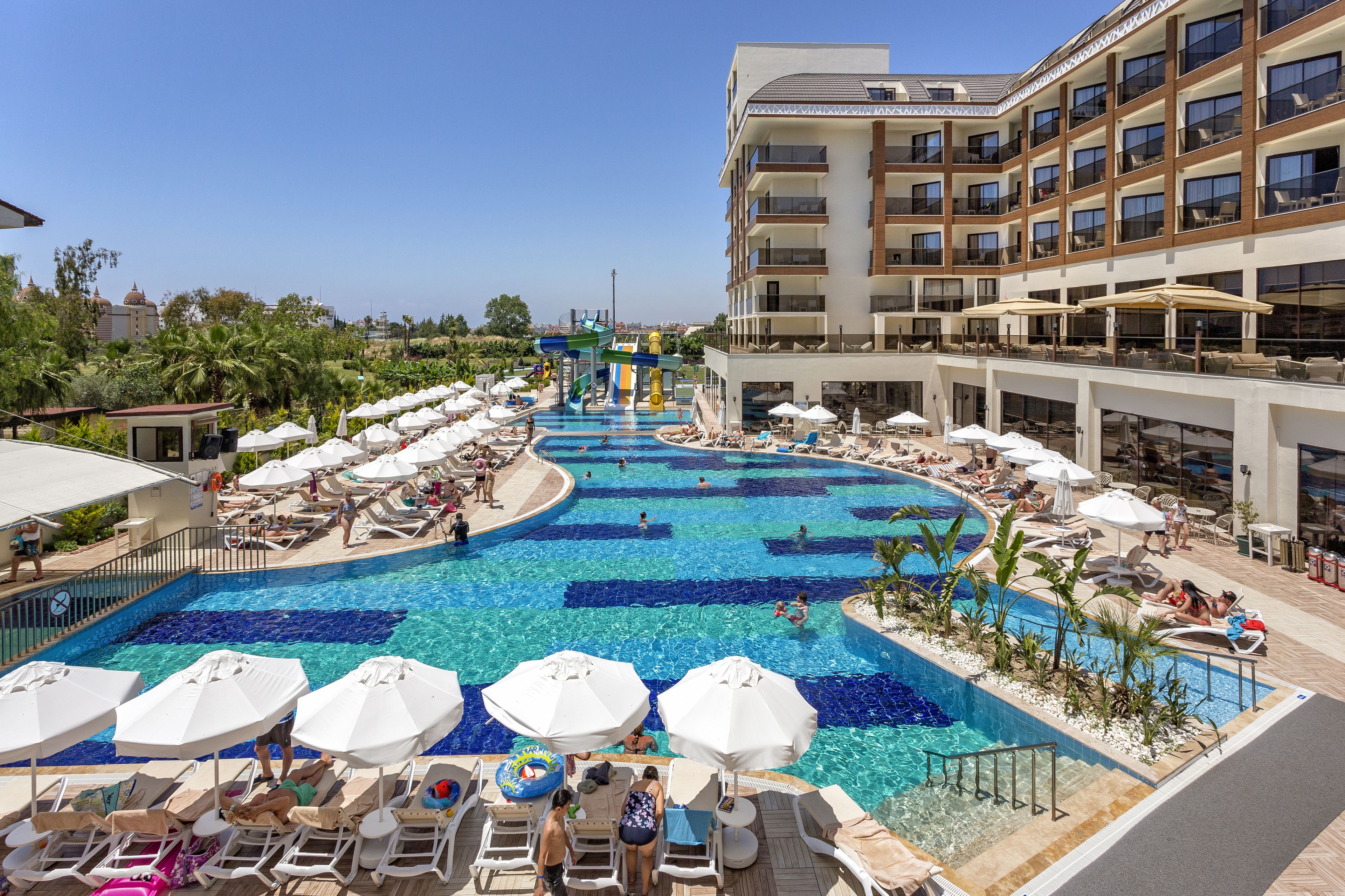 Un espace piscine d’hôtel doté de plusieurs niveaux de balcons, de chaises longues et de parasols.