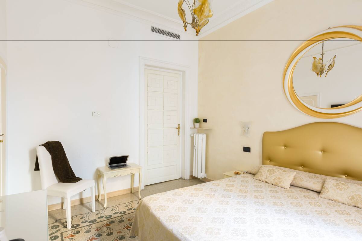 A bedroom with a bed, a chair, a desk, a mirror, and a radiator.