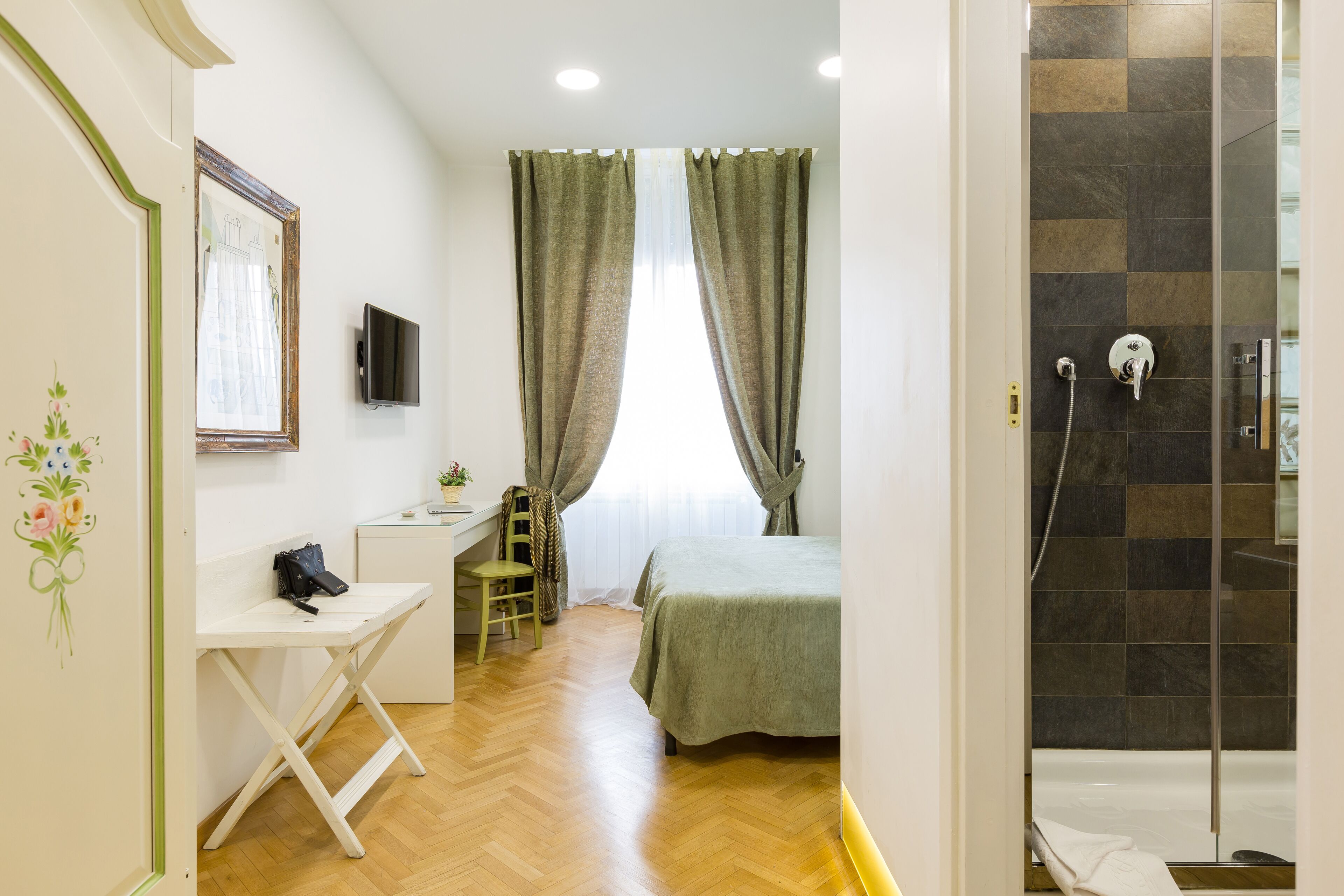 A room with a bed, desk, chair, and a shower area with a glass door.