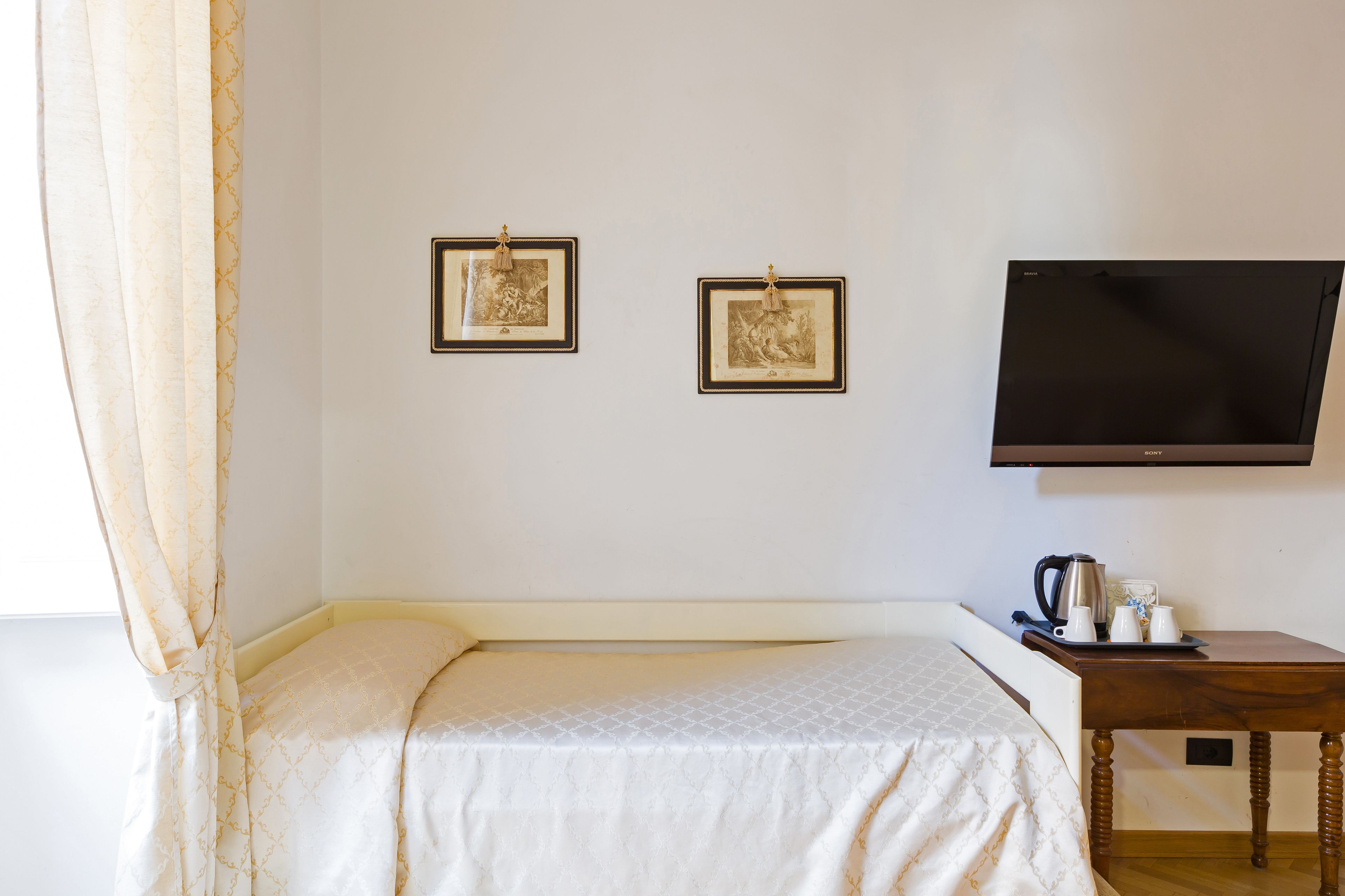 A hotel room with a bed, a flat-screen TV, and two framed pictures on the wall.