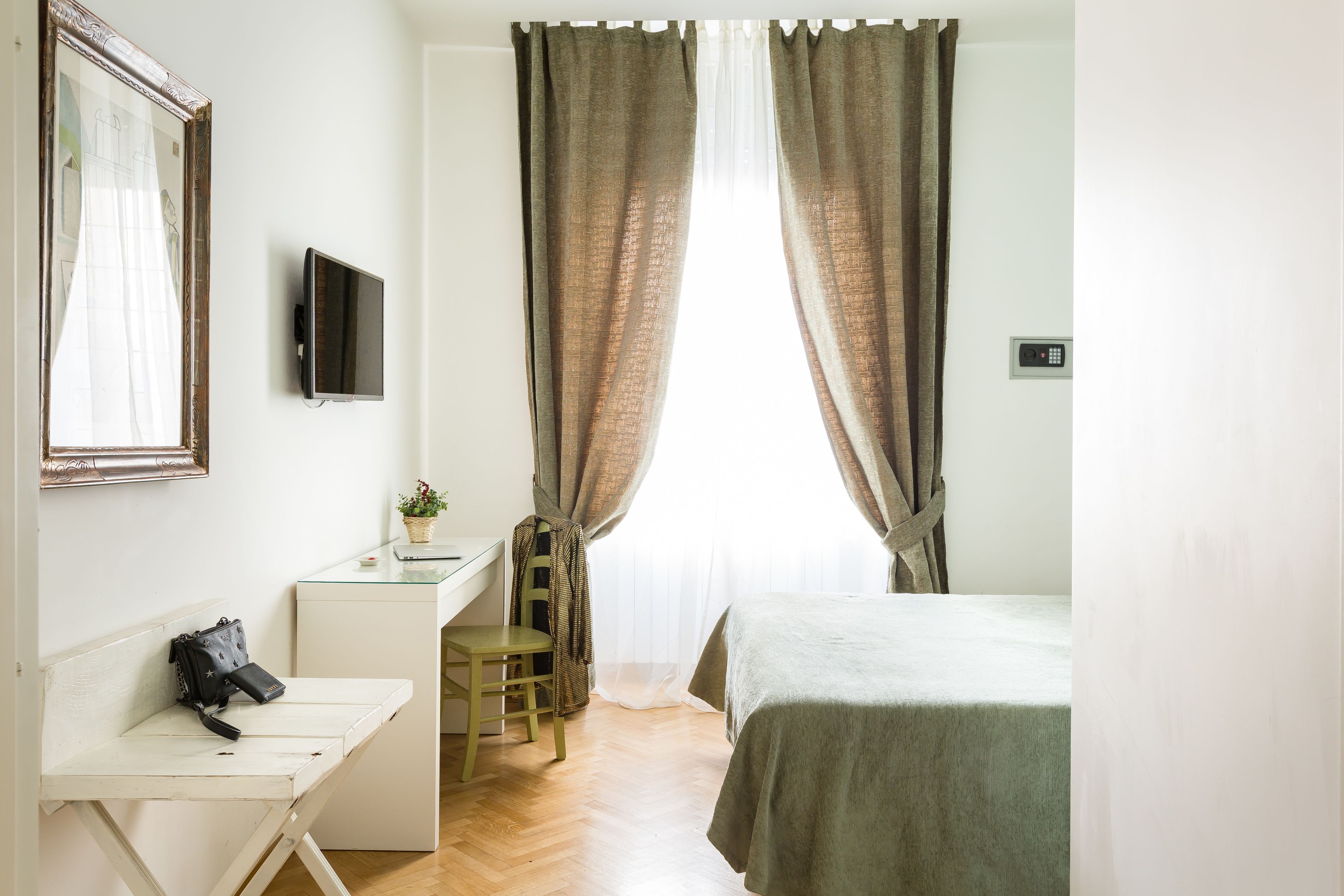 A room with a bed, a desk with a chair, a television, and a window with curtains.