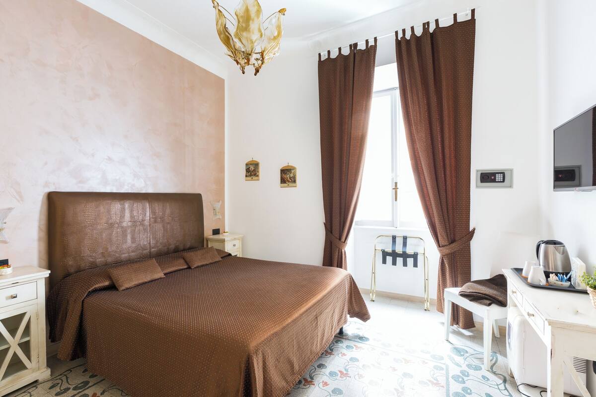 A bedroom with a large bed, a desk, a chair, a television, and curtains.