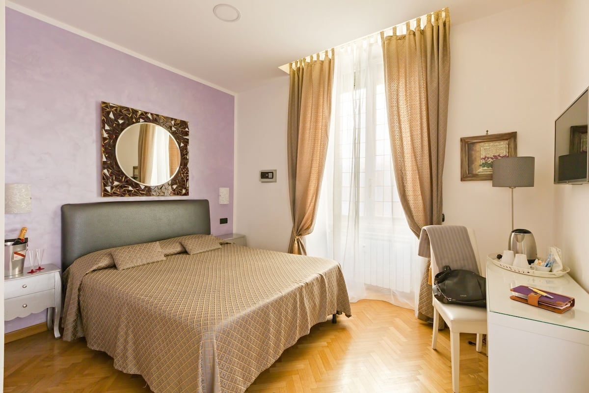 A neatly arranged bedroom with a bed, a chair, a desk, and a window with curtains.