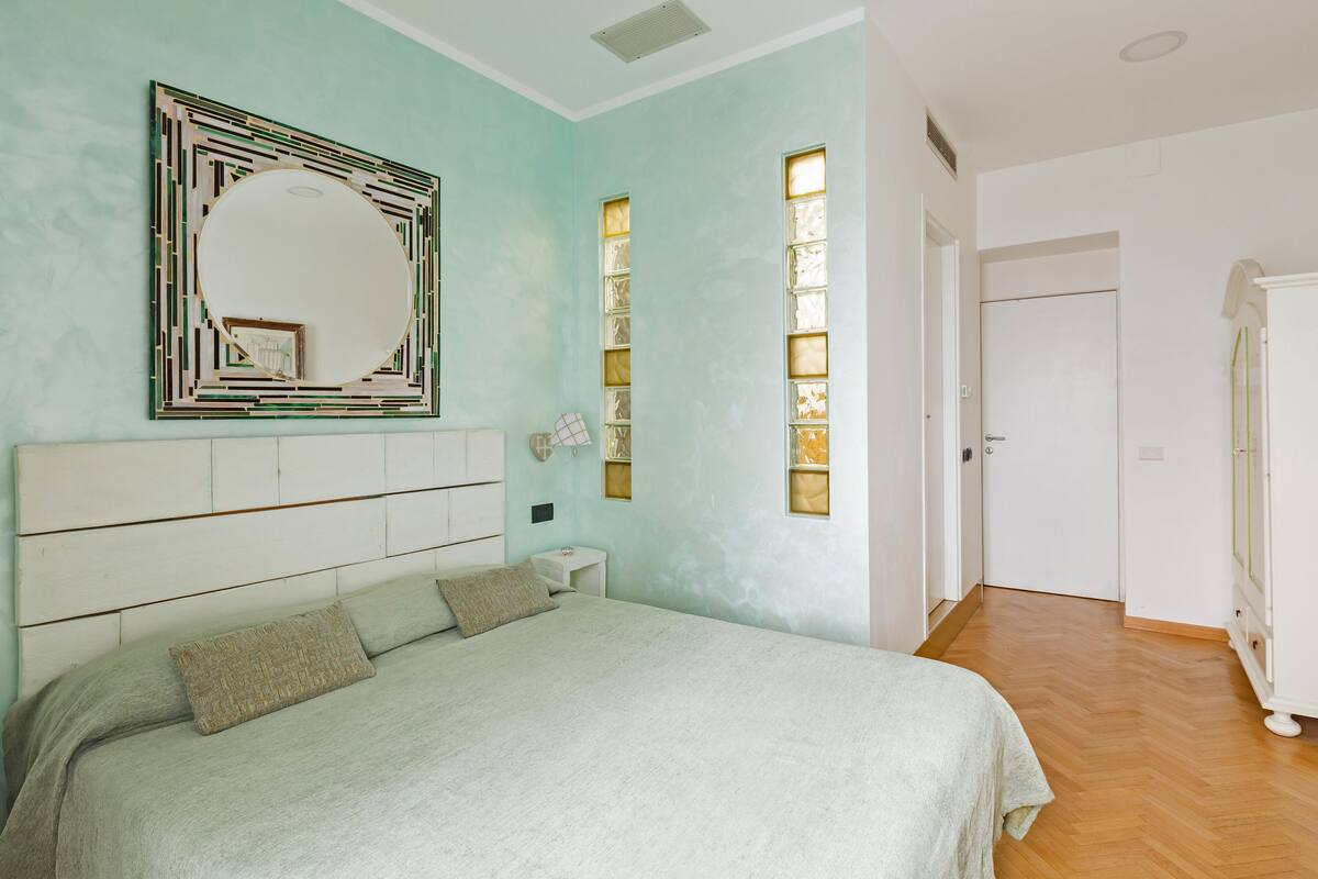A bedroom with a bed, a bedside table, a mirror, and a wardrobe.