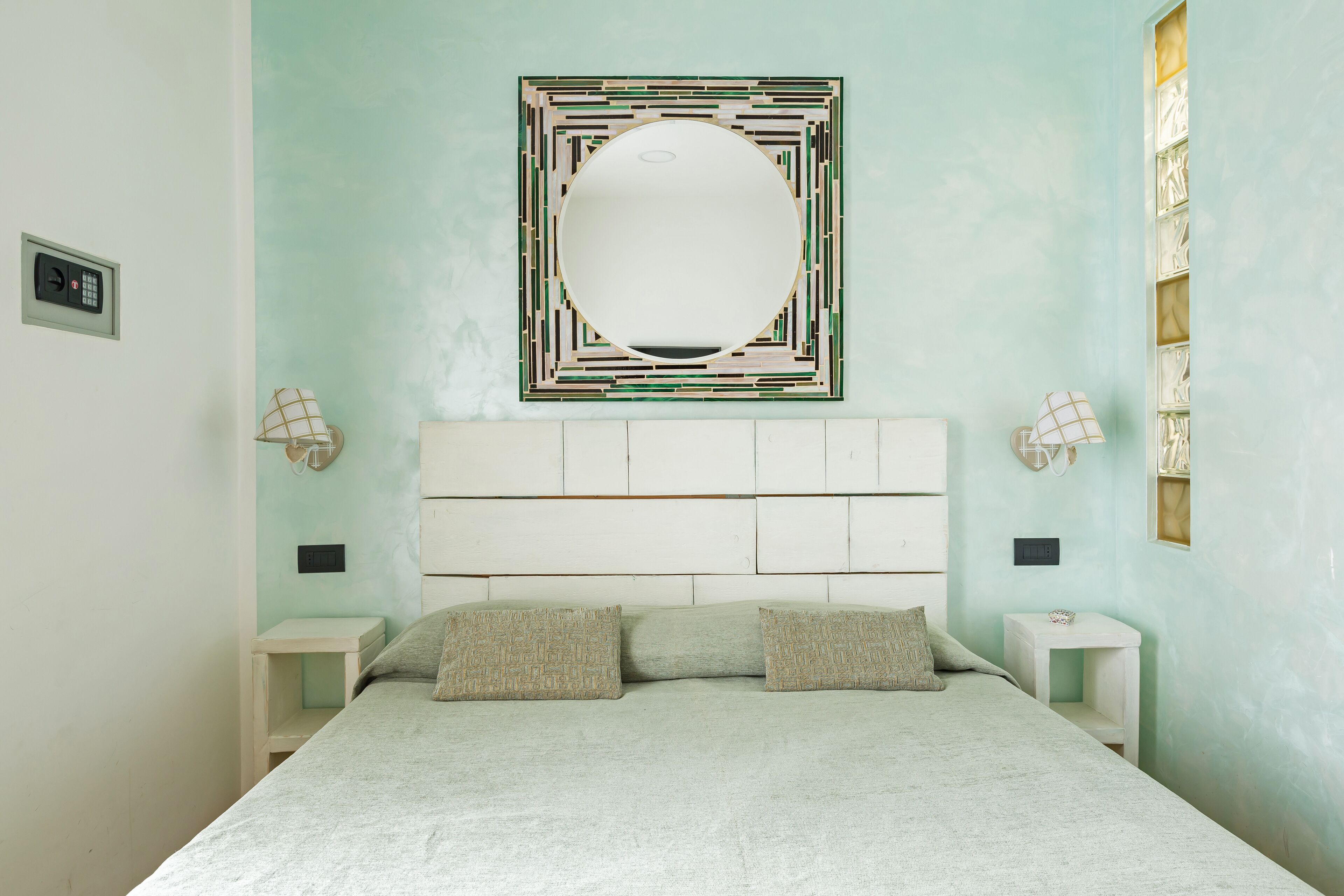 Une chambre à coucher comprenant un lit, deux tables de chevet, un miroir fixé au mur et un luminaire.
