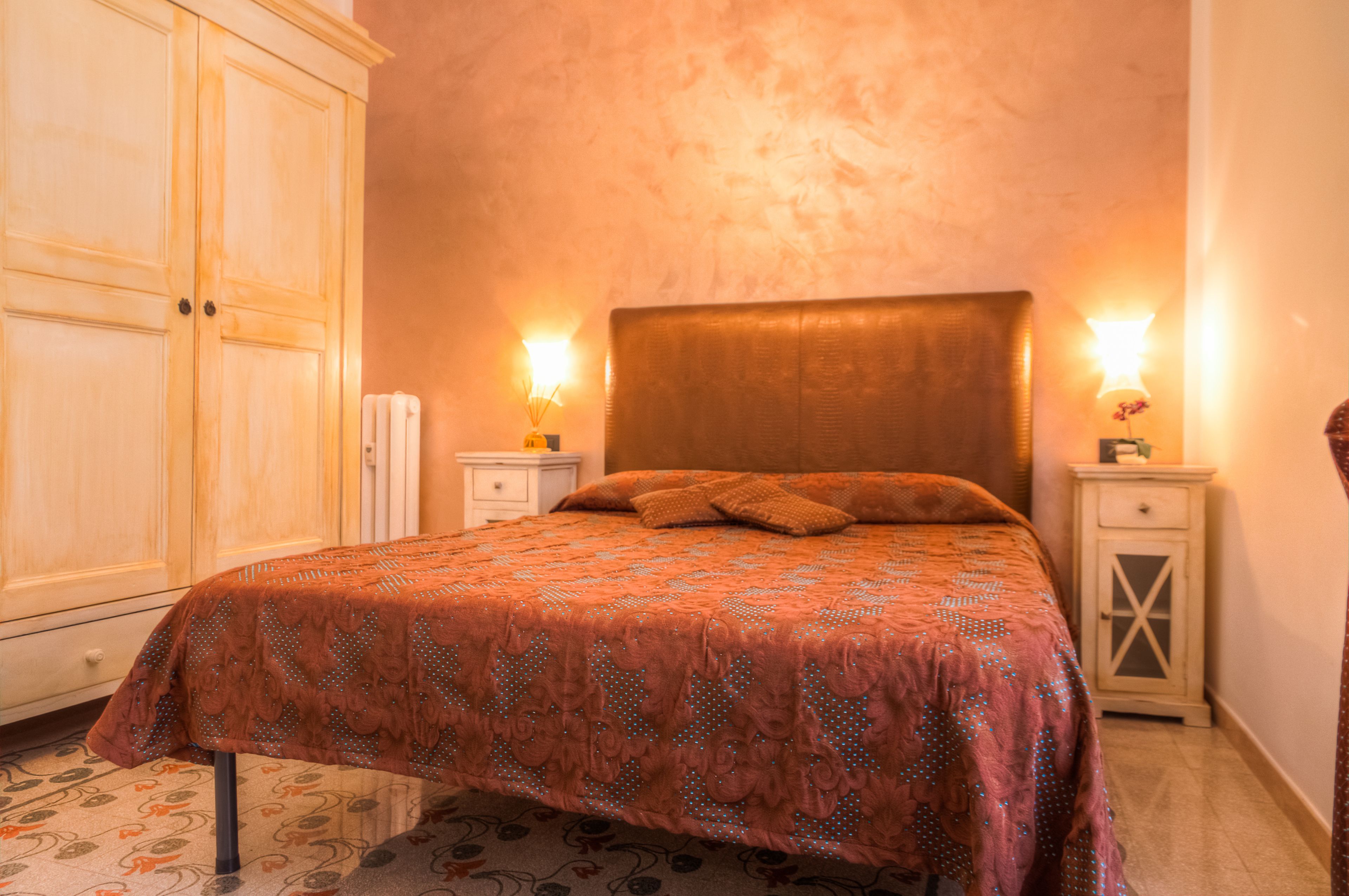 A bedroom with a bed, nightstands, a wardrobe, and a patterned carpet.