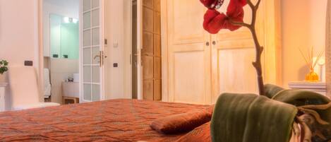 A hotel room with a bed, a wooden wardrobe, a mirror, and a plant.
