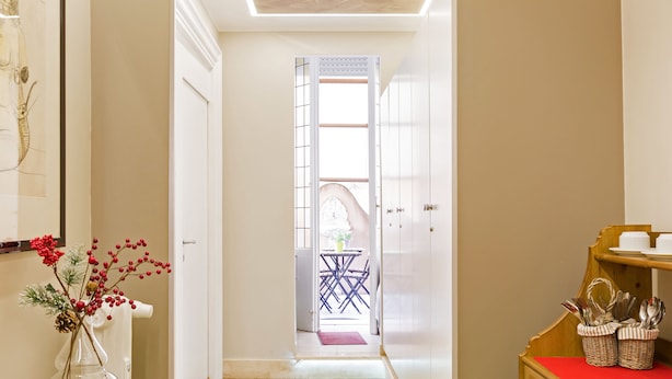A hallway with a wooden floor, a glass vase with red berries, and a table with baskets. - Relais Calamatta (Rome)