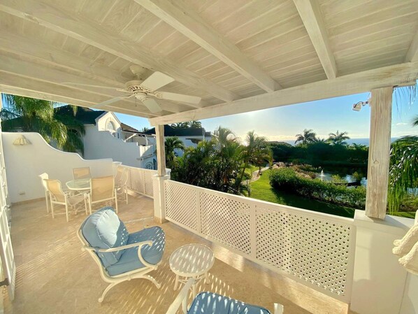 A covered outdoor seating area with a view of a landscaped garden and a body of water.
