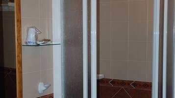 Un baño con lavamanos blanco, cabina de ducha de vidrio y espejo con marco de madera.