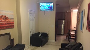 A living room with a black sofa, a television mounted on the wall, a door, and a kitchen area with a refrigerator. - DC International Hostel 2 (Washington)