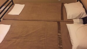 Two single beds with brown bedding and white pillows, a black metal headboard, and a white wall with a power outlet. - DC International Hostel 2 (Washington)