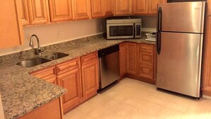 A kitchen with wooden cabinets, a stainless steel refrigerator, a microwave, and a dishwasher. - DC International Hostel 2 (Washington)