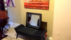 A room with a black cushioned bench, a framed mirror, and a painting of a sunset with the text "CALIFORNIA REPUBLIC". - DC International Hostel 2 (Washington)