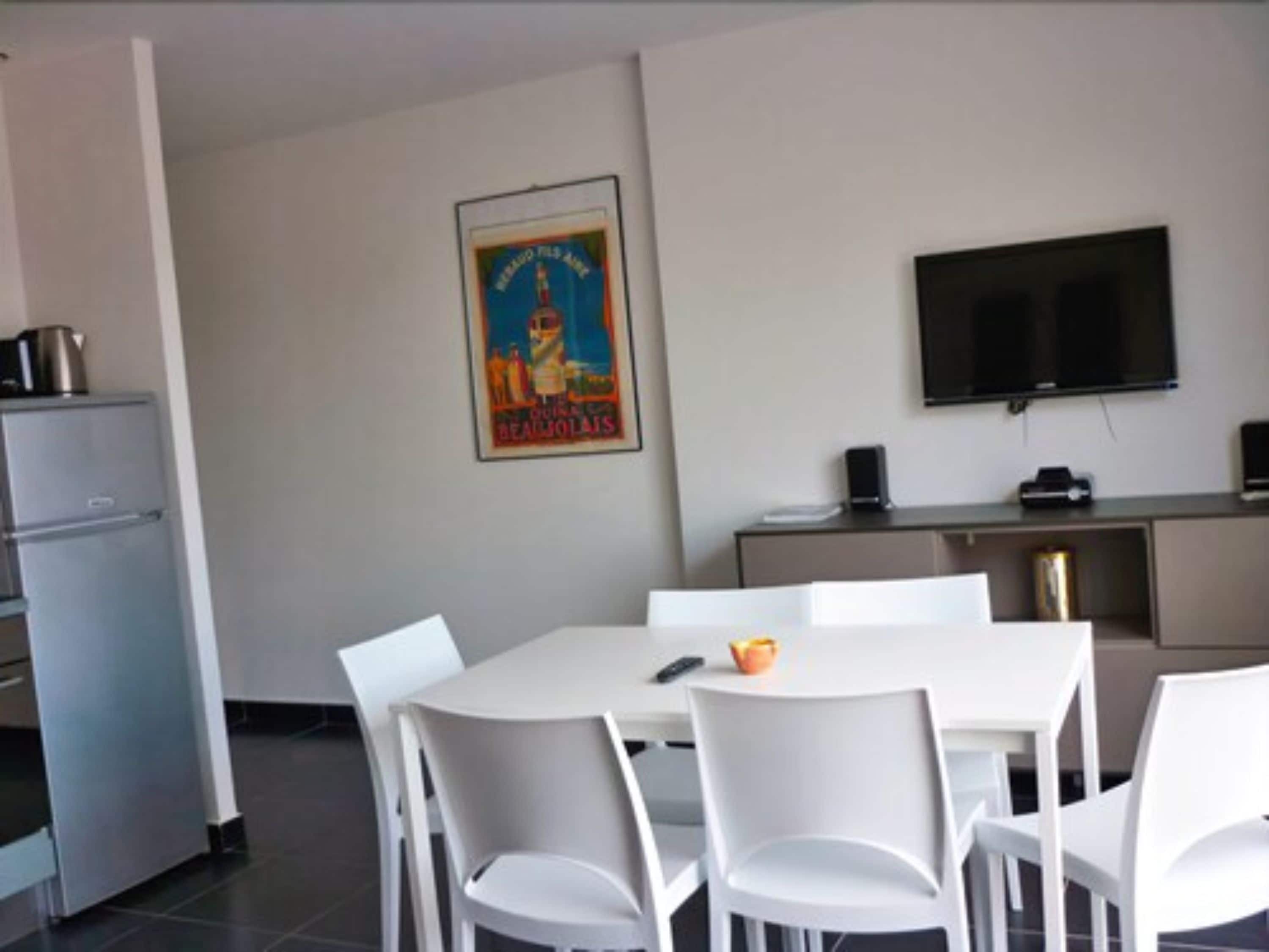 Una cocina moderna con electrodomésticos blancos, un comedor con sillas blancas, un televisor de pantalla plana y un cartel en la pared.