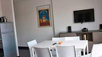 A modern kitchen with white appliances, a dining area with white chairs, a flat-screen TV, and a poster on the wall.