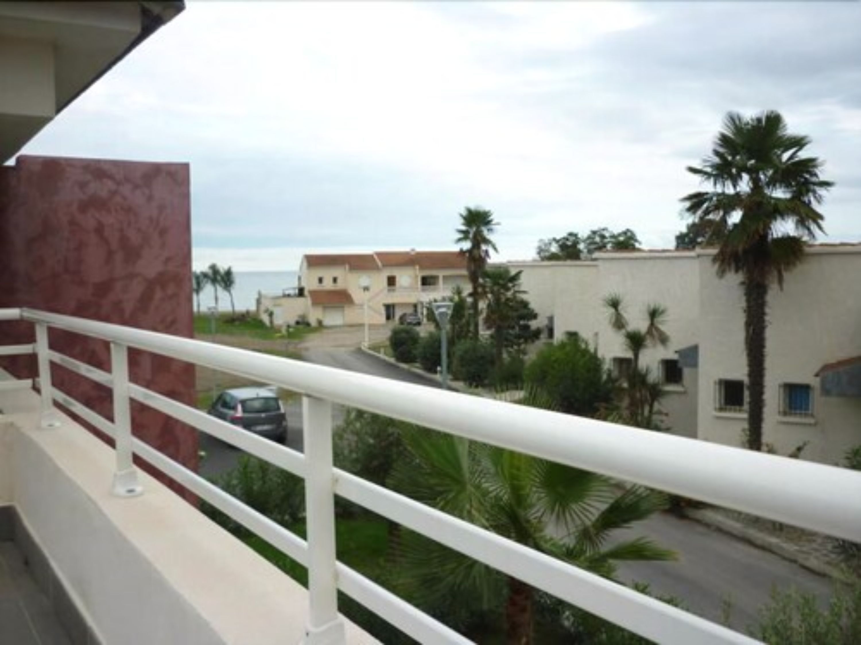 Un balcón con barandilla blanca que da a una zona residencial con palmeras y casas.