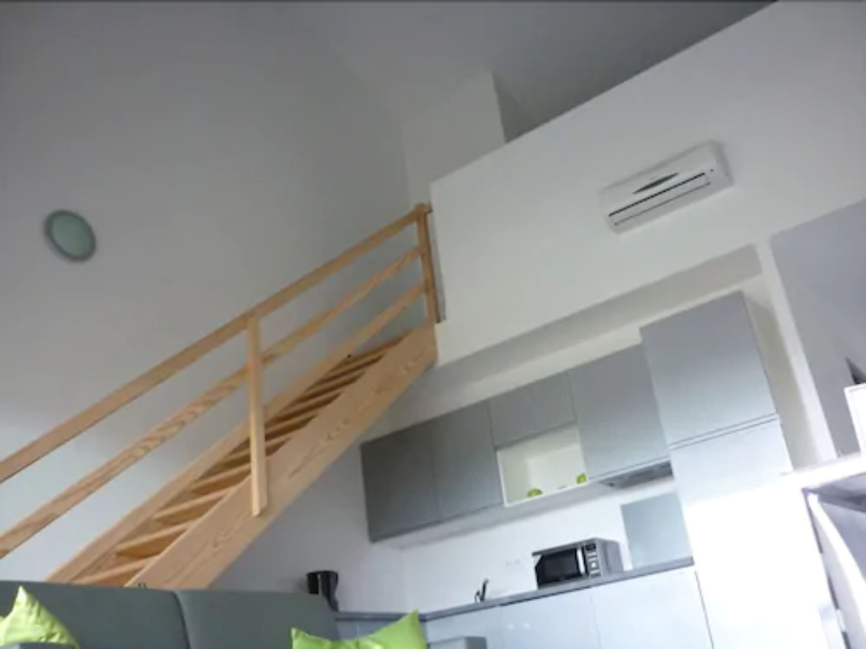 A modern kitchen with grey cabinets, a microwave, and a wooden staircase.
