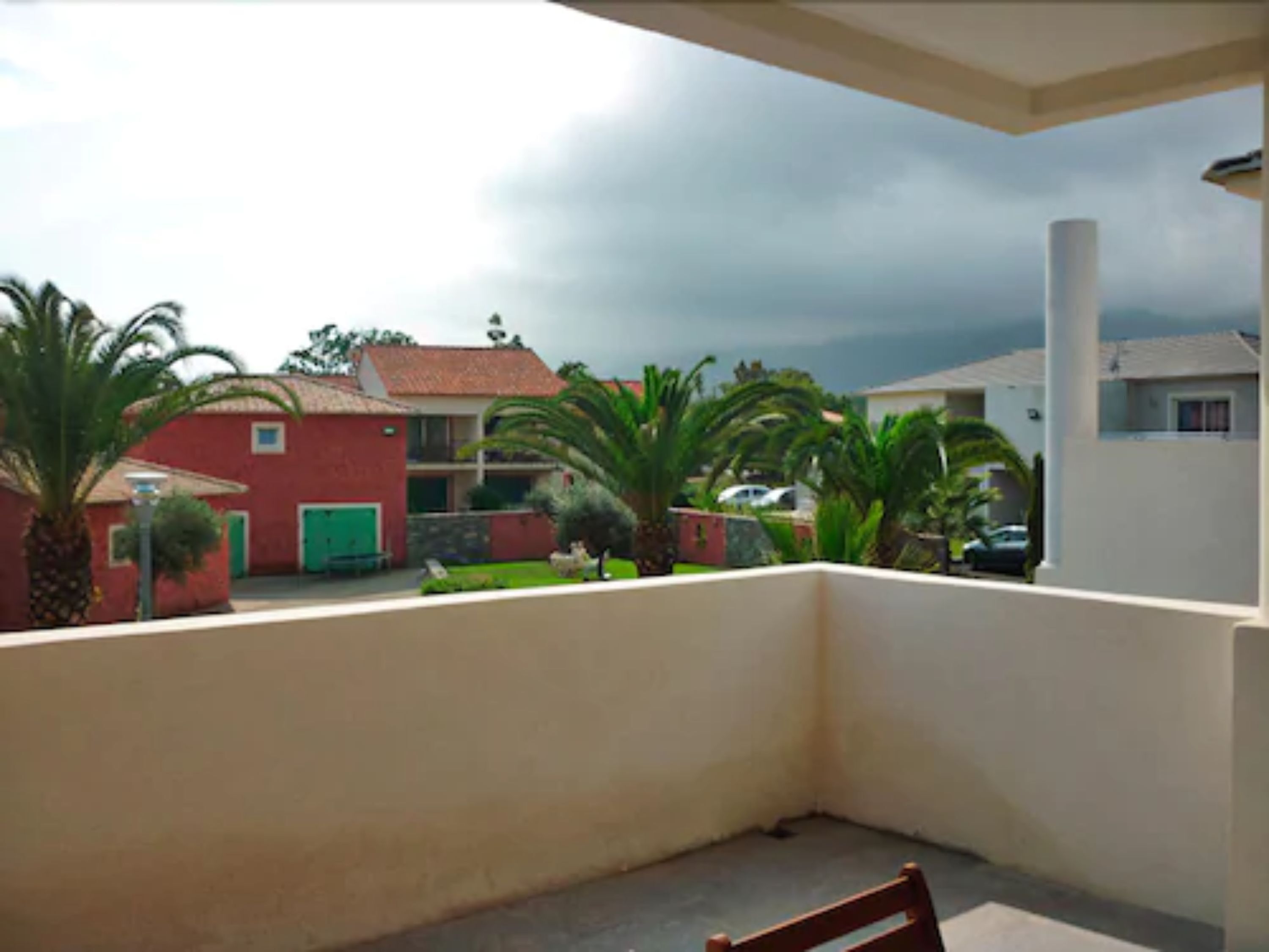 Un balcón con vista a casas vecinas y palmeras.
