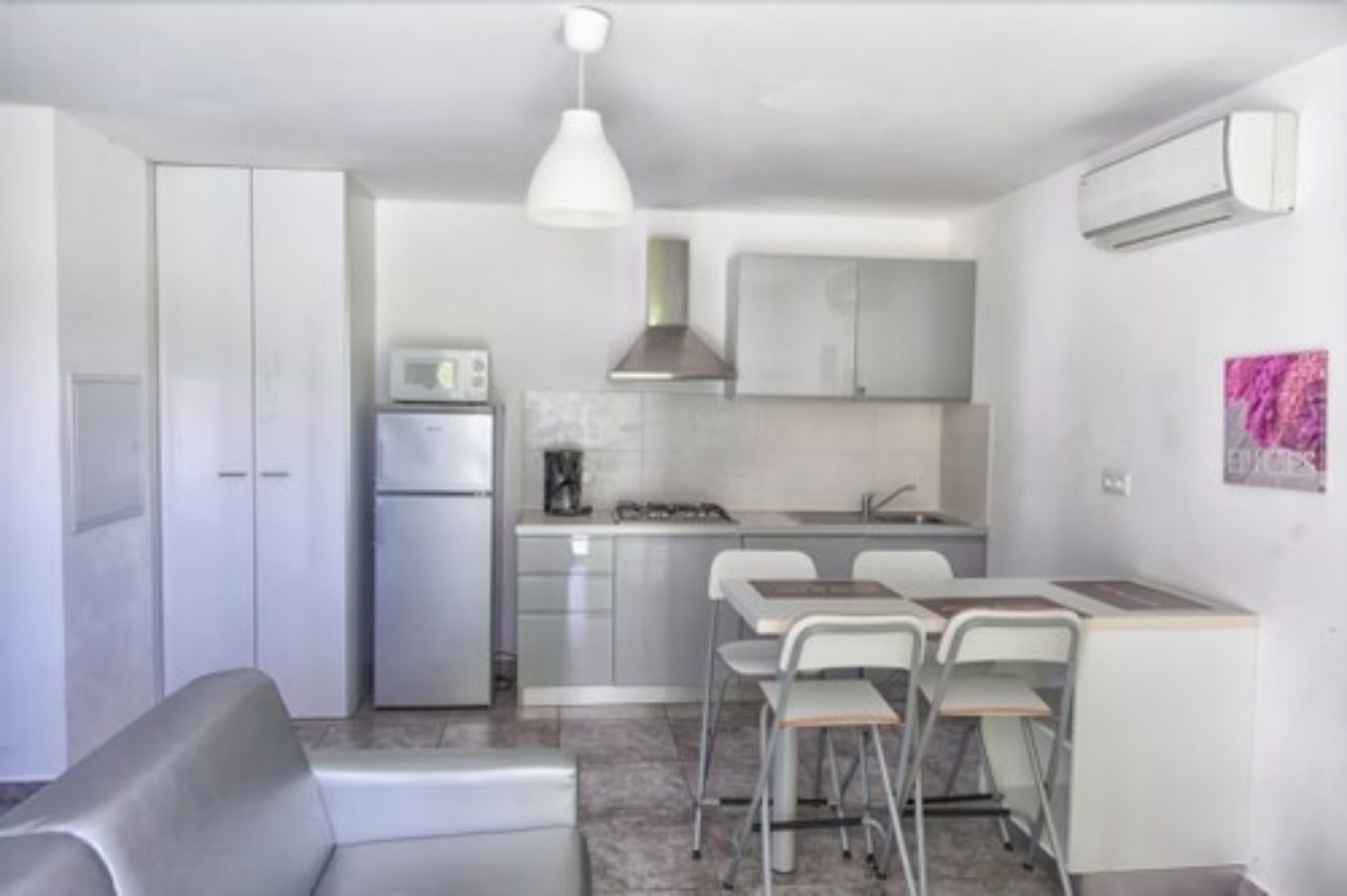 A compact kitchen with a refrigerator, stove, and white cabinets. There is a dining area with a table and chairs.