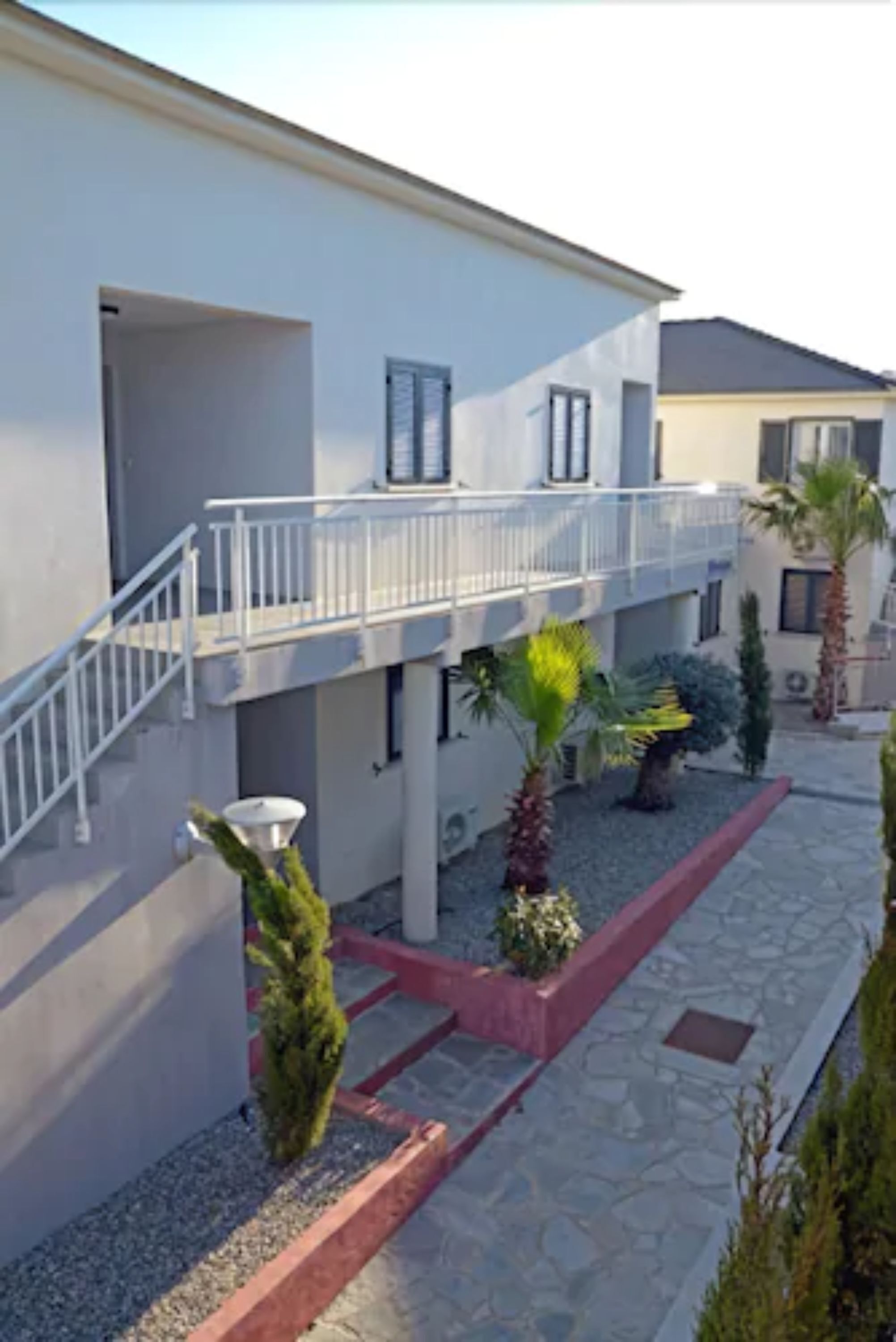 A modern building with a balcony, stone flooring, and potted plants.