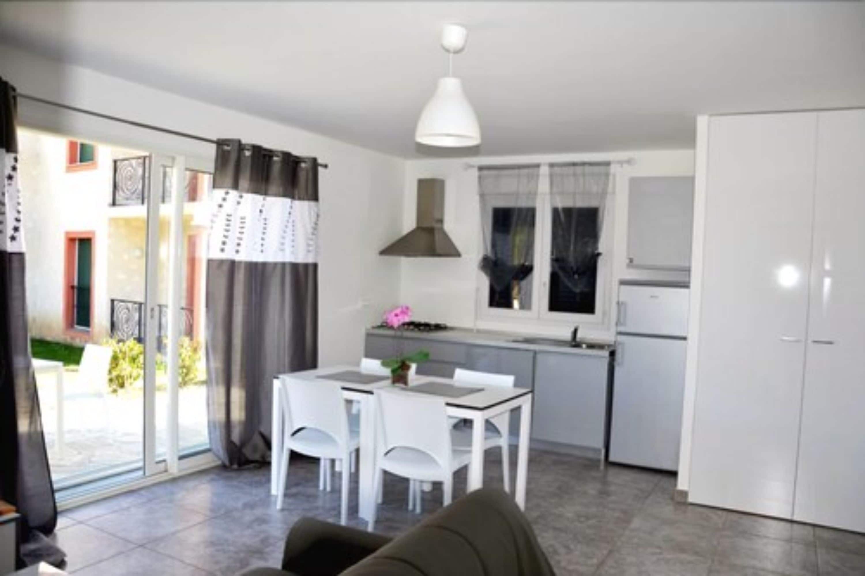 Une cuisine moderne avec des meubles blancs, un coin repas comprenant une table et des chaises, et une porte-fenêtre coulissante donnant sur un espace extérieur.