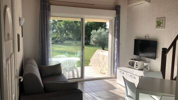 A living room with a sofa, a dining table, a TV, and a sliding glass door leading to a patio with outdoor furniture.