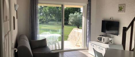 Una sala de estar con sofá, mesa de comedor, televisor y puerta corrediza de vidrio que da a un patio con mobiliario exterior.