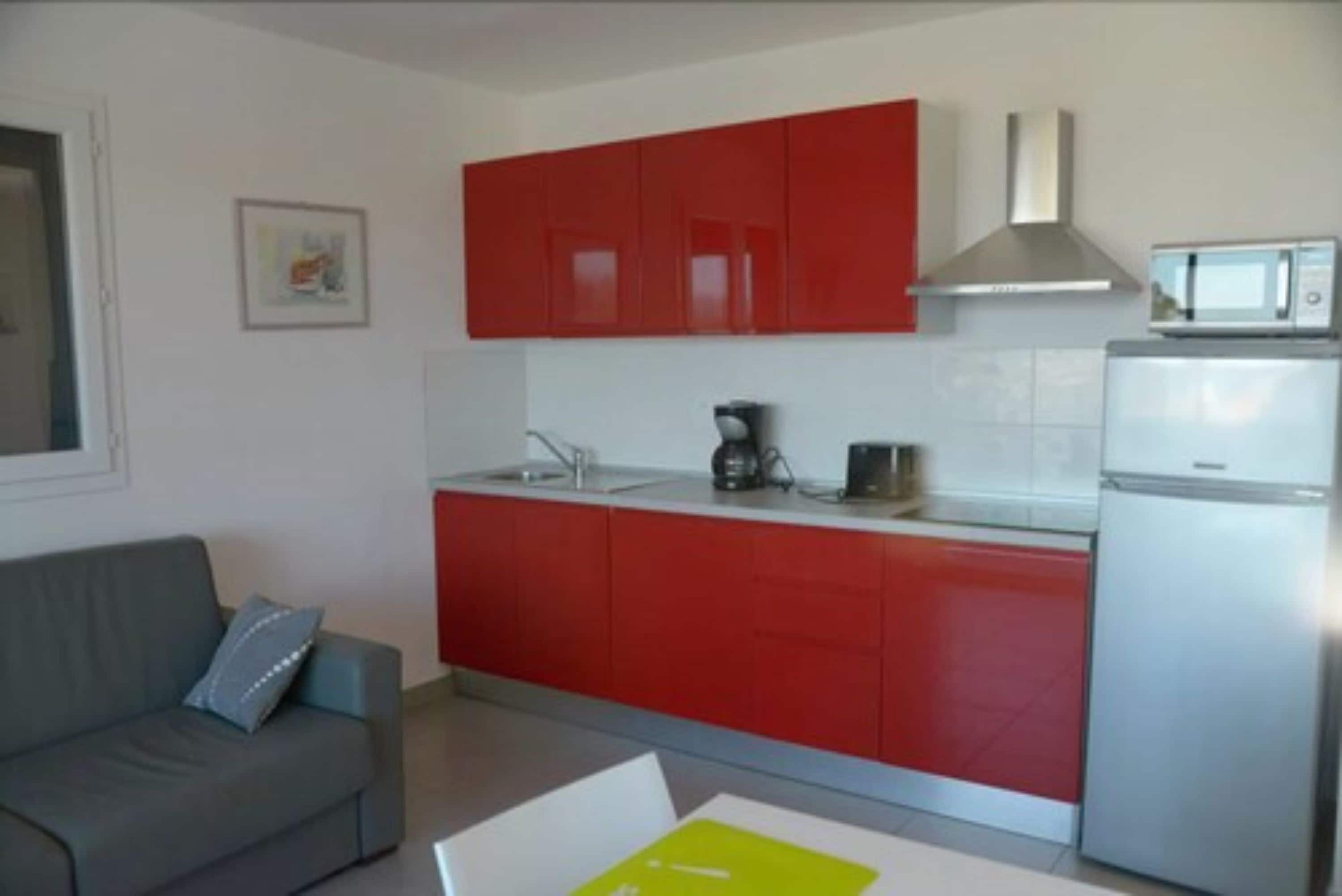 Una cocina compacta con armarios rojos, una encimera blanca, una campana extractora de acero inoxidable, un microondas y un refrigerador.