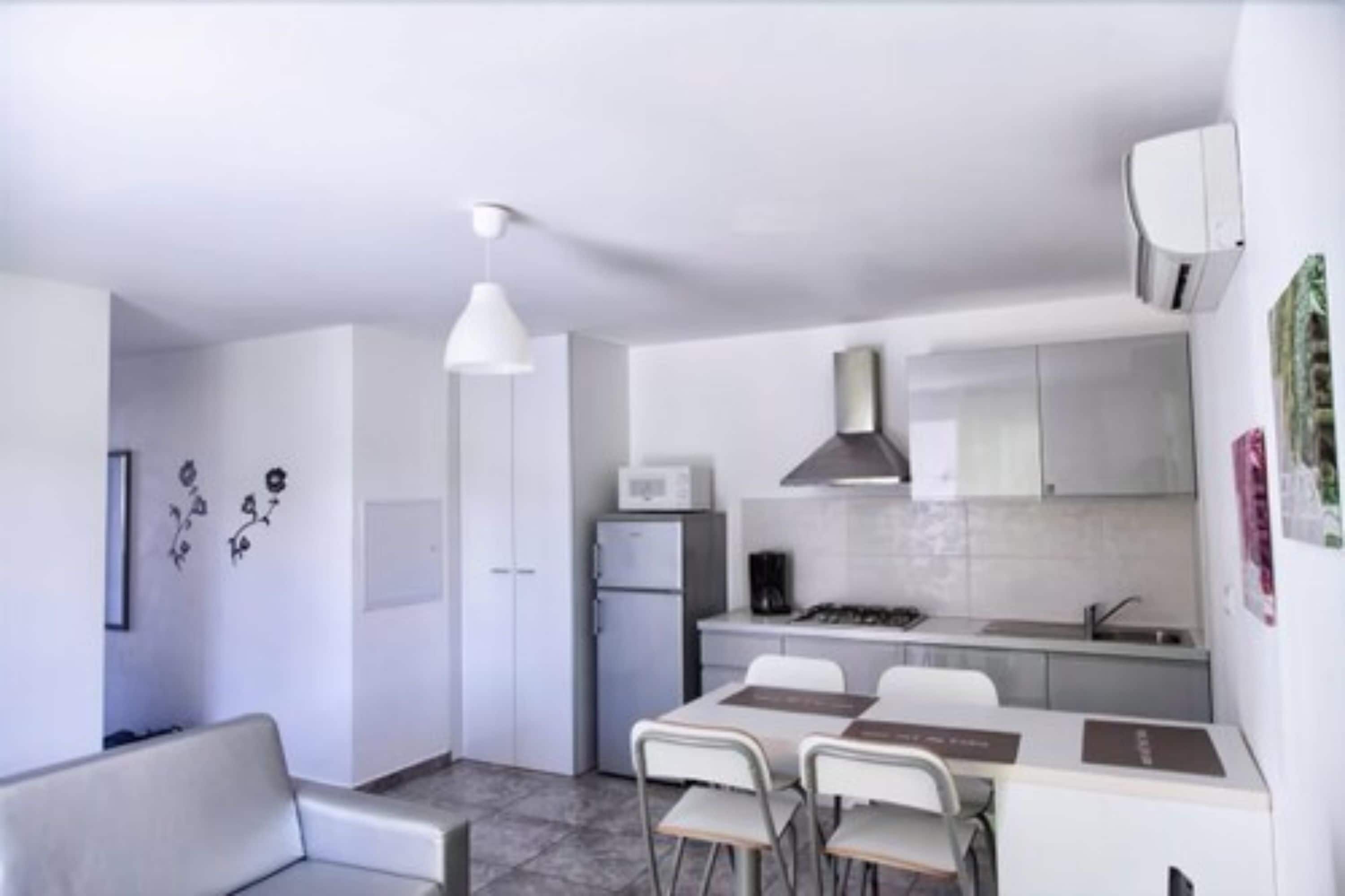 Cocina funcional con armarios blancos, microondas y estufa a gas. Zona de comedor con mesa y sillas.