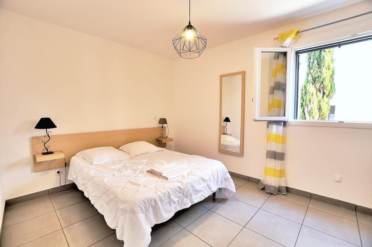 Una camera da letto con un letto, lampade ai comodini, un lampadario, una finestra con tende e uno specchio.