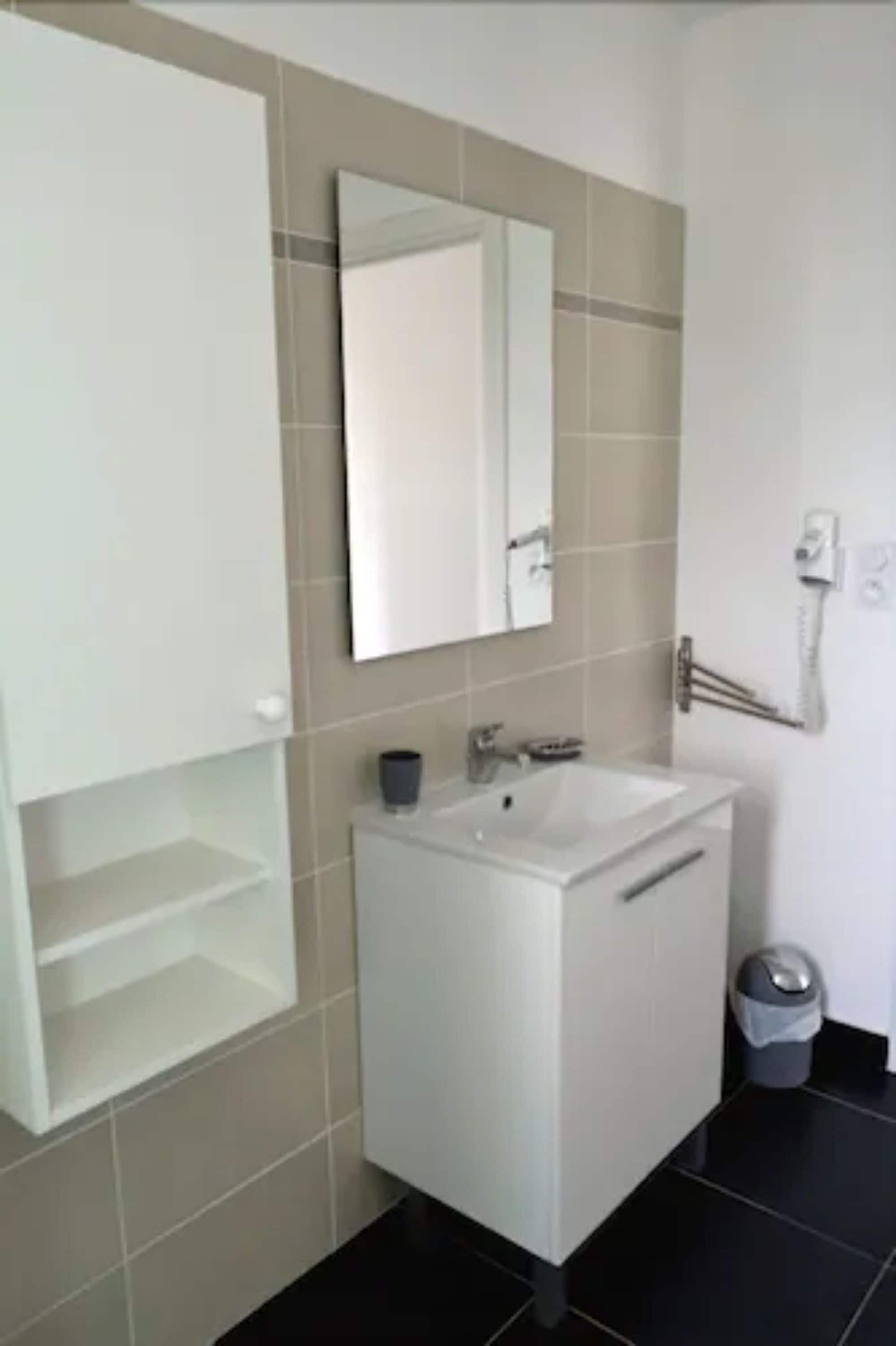 Un bagno con lavandino, specchio e mobiletti bianchi.