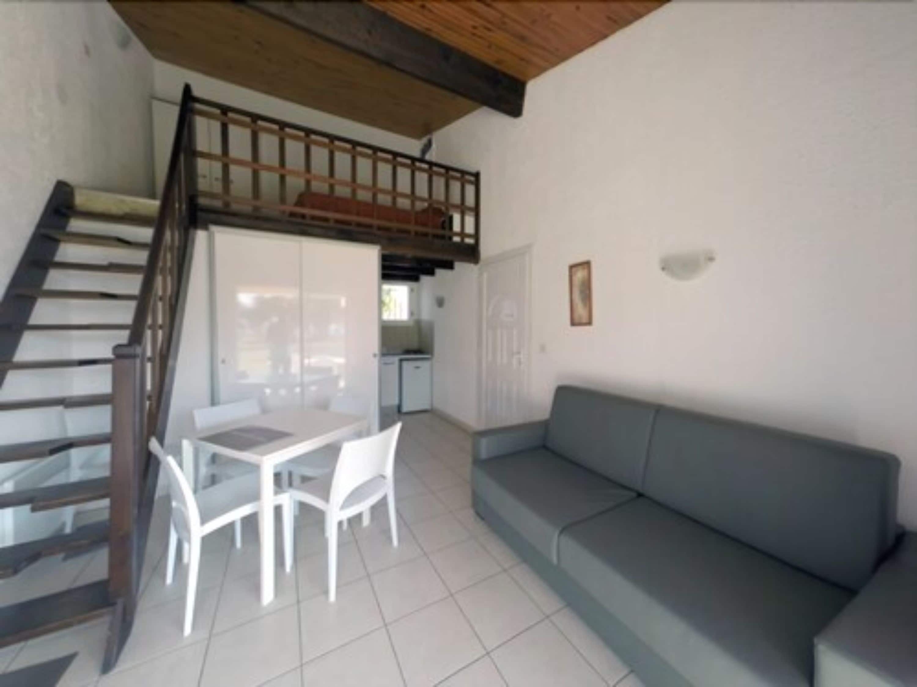 A compact living space with a staircase leading to an upper level, a dining area with a table and chairs, and a sofa.
