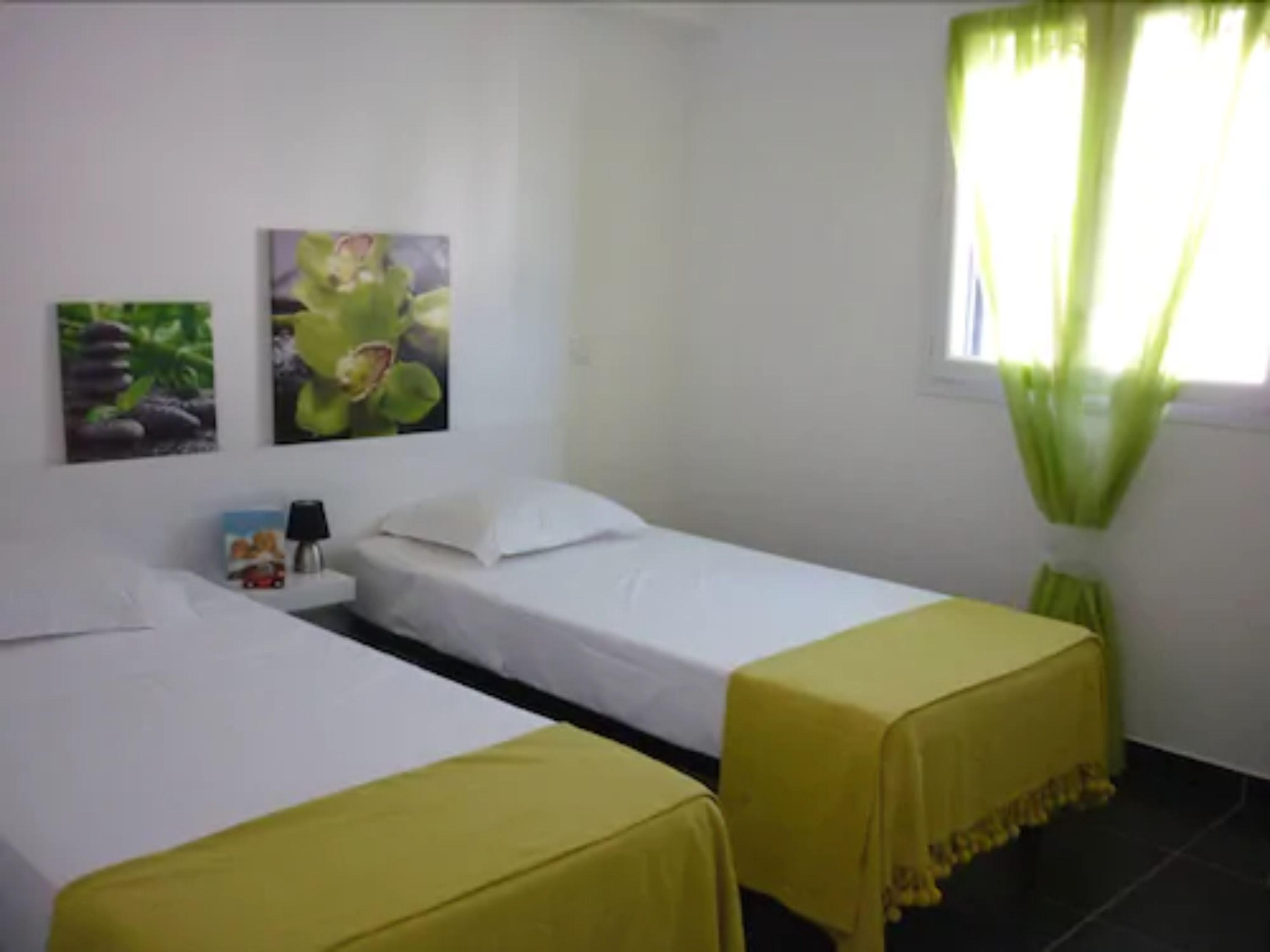 Una habitación con dos camas, una mesita de noche, una lámpara y dos cuadros colgados en la pared.
