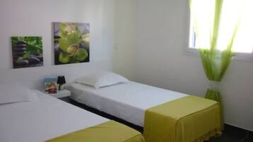 Una habitación con dos camas, una mesita de noche, una lámpara y dos cuadros colgados en la pared.