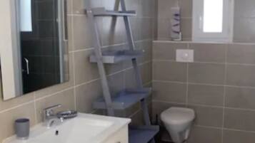 Une salle de bain avec un lavabo blanc, un miroir, des toilettes et une étagère.
