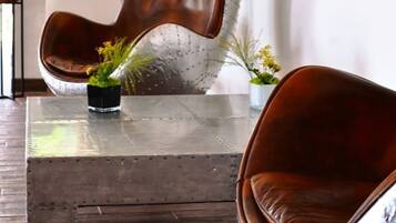 Una sala de estar moderna con un sillón escultural único, una mesita con una planta y un cuadro abstracto colorido en la pared.