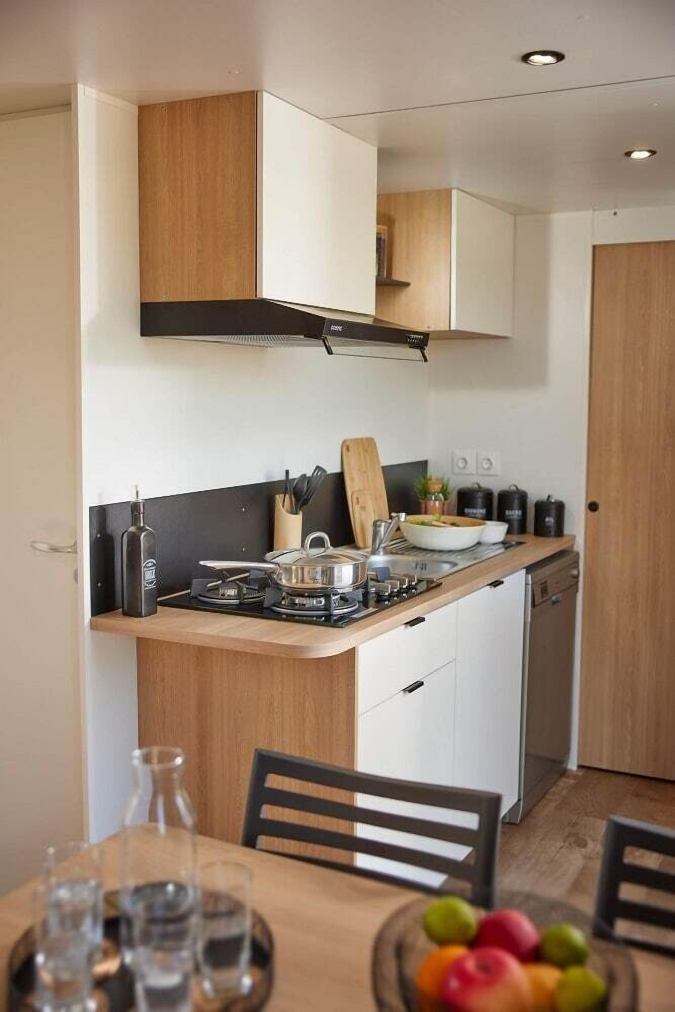Eine kompakte Küche mit Holz Arbeitsplatte, einem Gasherd, einem Geschirrspüler und einem Essbereich mit Tisch für zwei Personen.