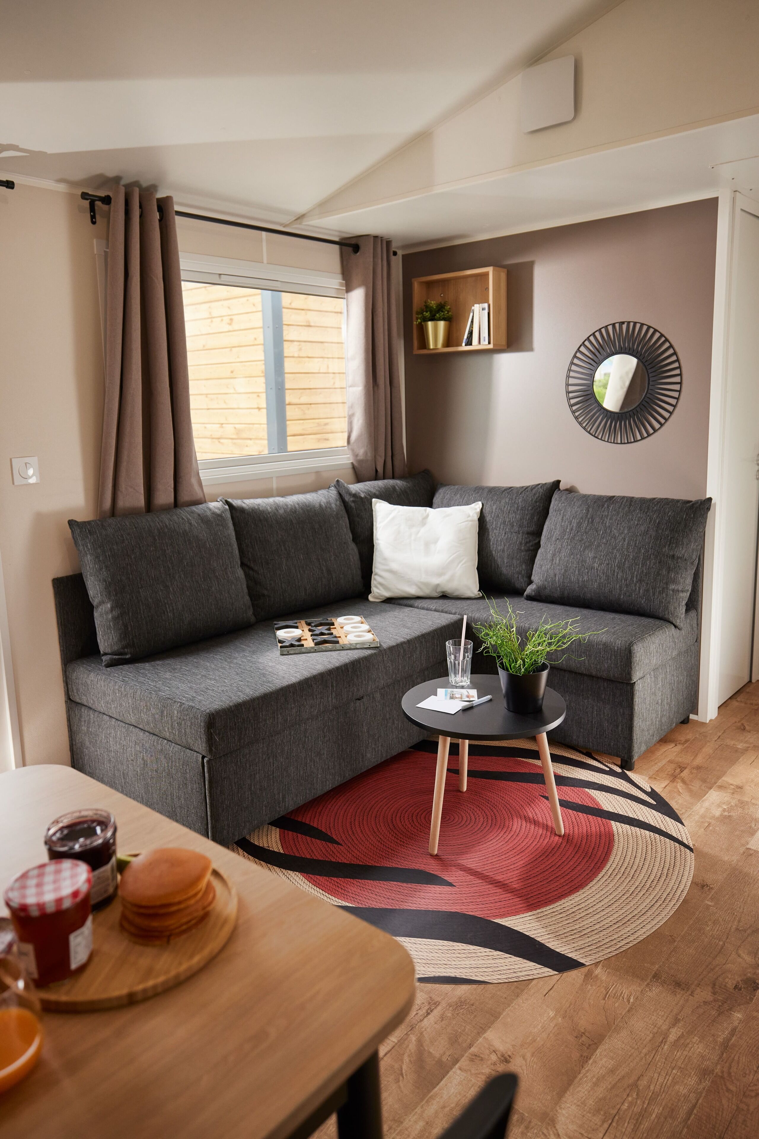 Una sala de estar moderna con un sofá seccional gris, una mesita redonda con una planta y un tapete rojo y negro.