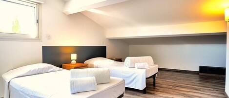 Habitación de hotel con dos camas, una mesita de noche con lámpara y suelo de madera.