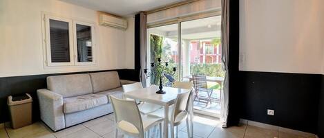 A modern living room with a sofa, dining table, chairs, and a balcony with a view.