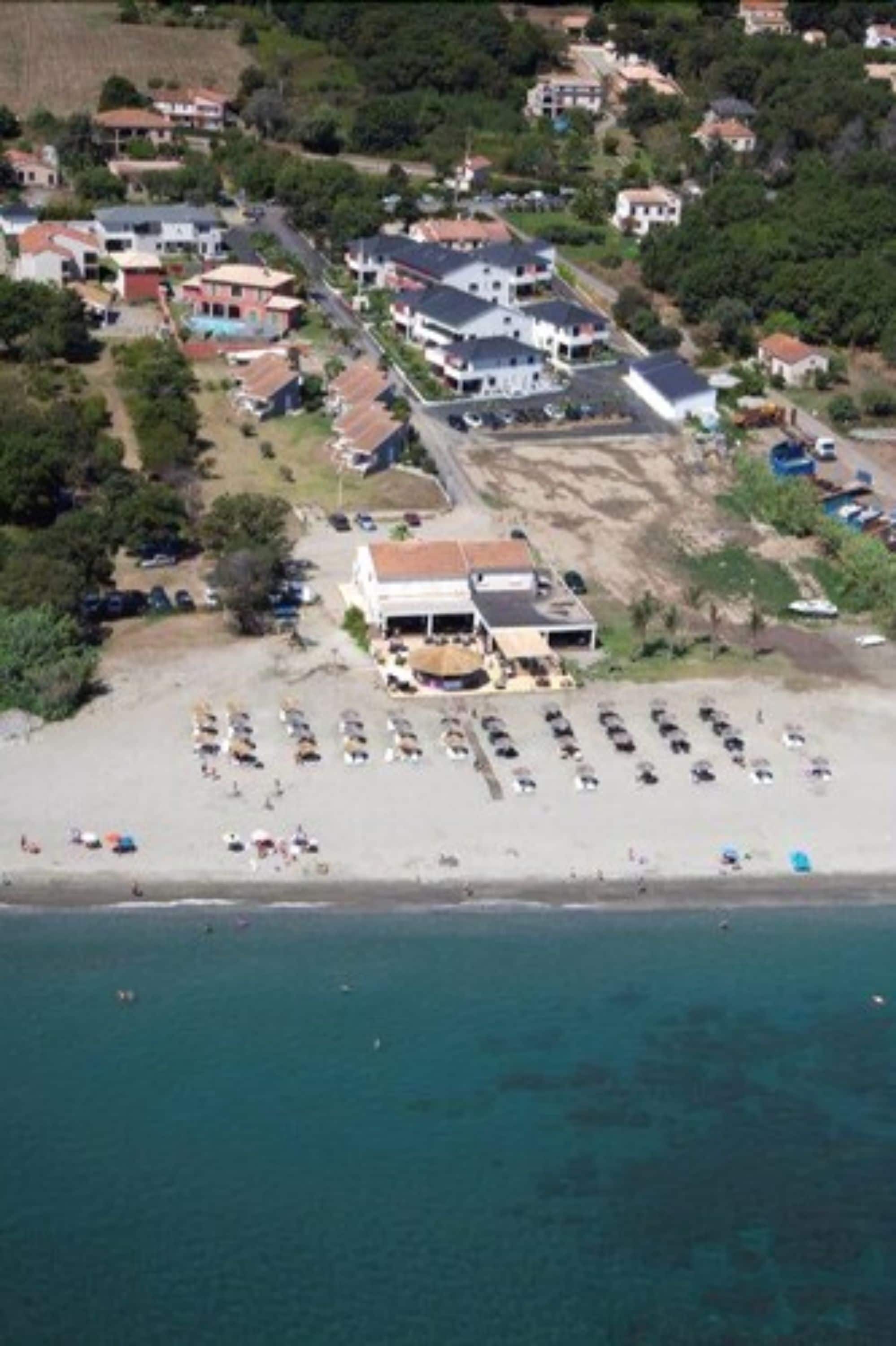 Vue aérienne d’un quartier résidentiel situé sur la côte, avec des maisons, une plage et un parking.