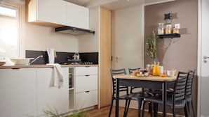 A modern kitchen with white cabinets, a wooden countertop, and a dining table with black chairs. There is a stove, a sink, and a hanging towel. - Résidence Marea Resort (Santa-Lucia-di-Moriani)