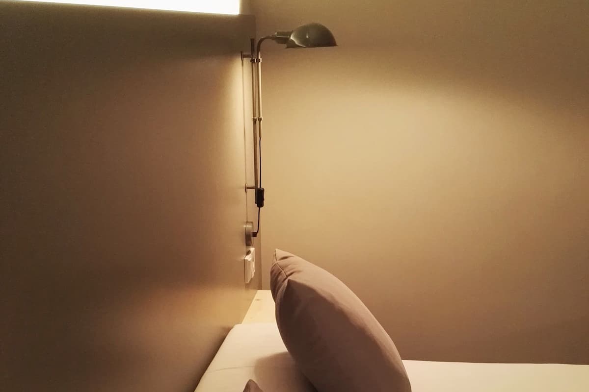 Een bed met twee kussens en een bedlampje in een kamer met beige wanden.