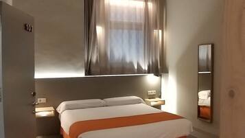 A bedroom with a bed, a window with curtains, a bedside table, and a mirror.
