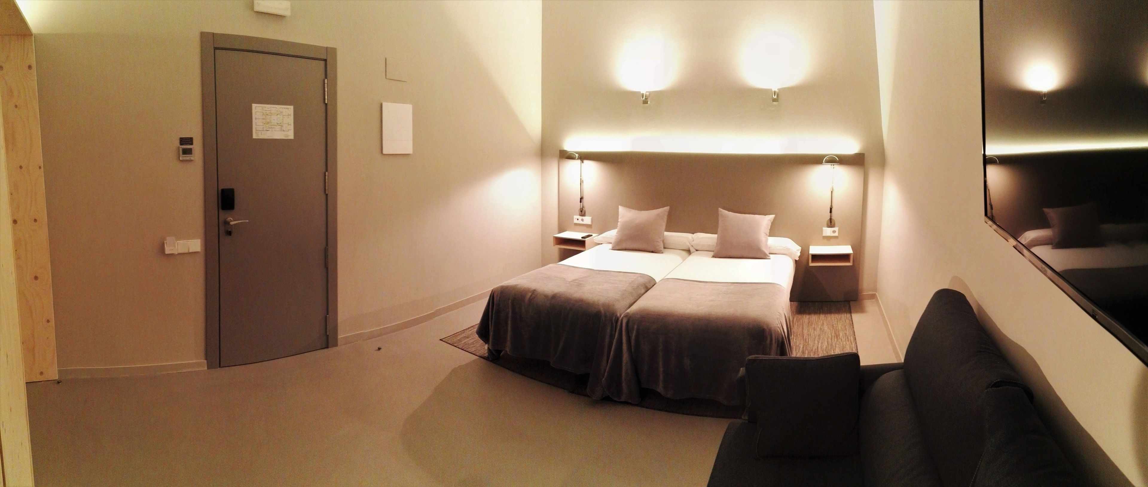 Habitación de hotel con cama, mesitas de noche, escritorio, una silla y una puerta.